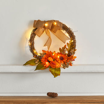 Decorative autumn wreath with orange flowers, greenery, berries, burlap bow and warm lights
