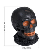 Black skull decoration with orange eyes and teeth on textured base, 15 cm tall