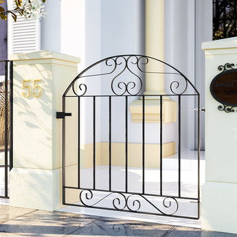 Black wrought iron pedestrian gate with arched top, scrollwork, and vertical bars.