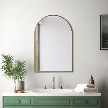 Arch-shaped gold-framed wall mirror above a green vanity and white sink