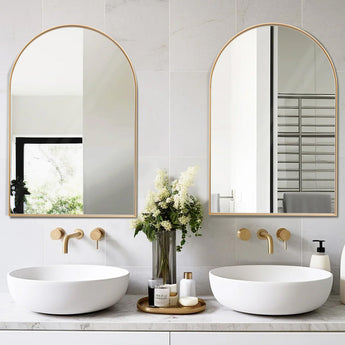 Pair of arch-shaped wall mirrors with gold metal frames above two sinks