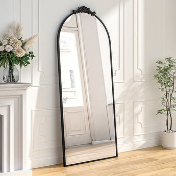 Black arched freestanding mirror with ornate metal top frame, full-length view