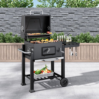 Portable charcoal BBQ grill with side shelf, wheels, and open lid; food on grates