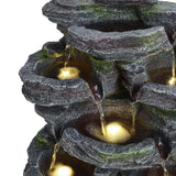 Faux rock garden fountain close-up, water pouring over tiers with warm light glow.