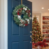 Snow-flocked Christmas wreath with pinecones, red berries and white ornaments on door