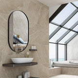 Black oval wall mirror with rounded arch frame, hanging above a bathroom sink.