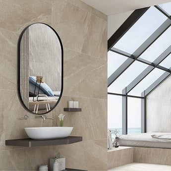 Black oval wall mirror with rounded arch frame, hanging above a bathroom sink.