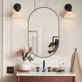 Black oval wall mirror with rounded arch frame above a white countertop and vase.