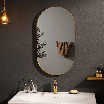 Gold oval wall mirror with thin frame in a dark bathroom wall setting.