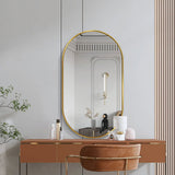 Gold oval wall mirror with slim metal frame over a wood vanity and plants.