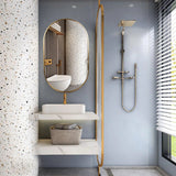 Gold oval wall mirror with thin frame in a modern bathroom with sink and shower.