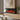 Recessed electric fireplace in wood wall, black glass front with red-orange flames