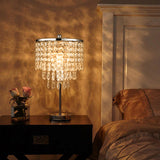 Small crystal table lamp with round base and dangling chandelier-style prisms