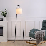 Metal tray table floor lamp with linen shade, black stand and circular top tray.