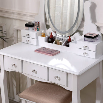 White makeup vanity desk with oval mirror, drawers, and cushioned stool below