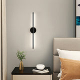 Black linear LED wall sconce with round backplate and vertical bar, white light