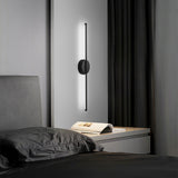 Black linear LED wall sconce with round backplate and vertical bar, white glow