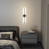 Black linear LED wall sconce with round backplate and vertical light bar, warm glow