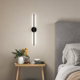 Black linear LED wall sconce with round backplate and vertical light bar, warm glow