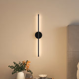 Black linear LED wall sconce with round backplate and vertical light bar, warm glow