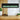 Black wall-mounted electric fireplace with green flame effect visible through the front glass.