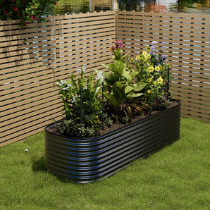 Oval raised garden bed planter in black with ribbed sides, holding flowering plants