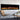 Black electric fireplace with orange flame bed glowing behind glass, wall mounted