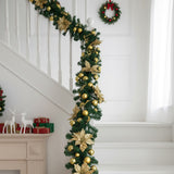 Green pine garland with gold ornaments and warm LED lights draped on white stair railing