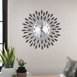 Decorative wall clock with round face, black numbers, silver crystal accents, and feather-like metal hands.