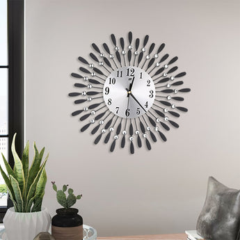 Decorative wall clock with round face, black numbers, silver crystal accents, and feather-like metal hands.