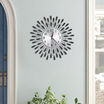 Sunburst metal wall clock with round dial, black numbers, and sparkling crystal drop accents.