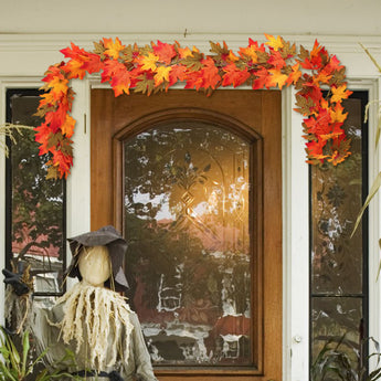 Maple leaf garland with warm lights, orange and yellow leaves across a window top