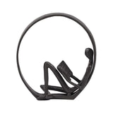 Close-up of metal man reading inside circular ornament figurine, dark finish