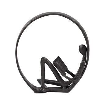 Close-up of metal man reading inside circular ornament figurine, dark finish