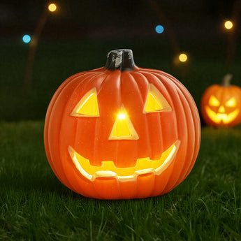 Orange LED pumpkin lantern on grass, jack-o'-lantern smile glowing from eyes and mouth