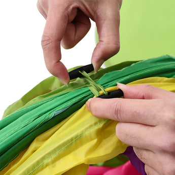 Hands fastening green and yellow sections with black strap on crawl tunnel