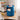 Blue round storage unit with two drawers, top compartment holding books and decor.