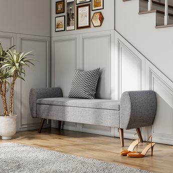 Grey linen upholstered storage bench with tufted base, rounded ends, and wooden legs