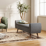 Grey linen storage bench with hinged lid and upholstered arms on wooden legs