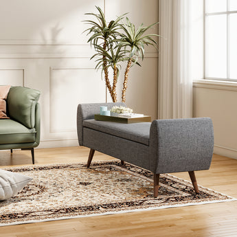 Grey linen storage bench with hinged lid and upholstered arms on wooden legs