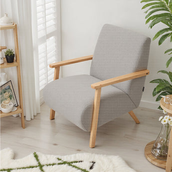 Grey chenille armchair side view: rounded armrests and tapered light wood legs.